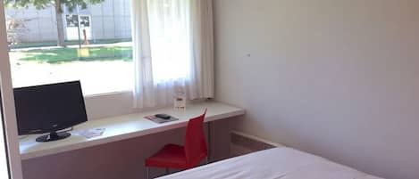 Une chambre d’hôtel avec un lit, un bureau équipé d’un ordinateur et d’une chaise, et une fenêtre avec des rideaux.