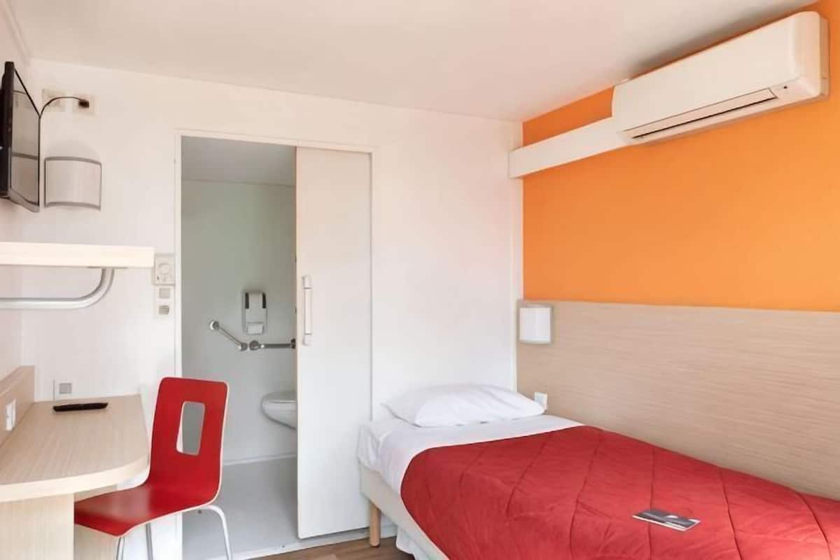 Quarto com beliche, uma escrivaninha com cadeira, casa de banho e unidade de ar condicionado.