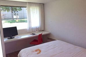 A hotel room with a bed, a desk with a computer, a chair, and a window with curtains. - Premiere Classe Poitiers Futuroscope - Chasseneuil (Chasseneuil-du-Poitou)
