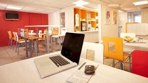 A modern office space with a laptop on a desk, a mobile phone, and a dining area with chairs and tables.