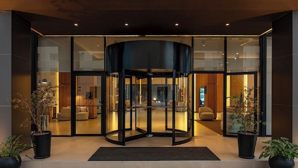 Une entrée d’hôtel moderne avec une porte tournante, des portes vitrées et un espace de réception visible à travers le verre.