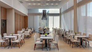 Un vaste espace dédié à la salle à manger, avec de nombreuses tables et chaises, de grandes fenêtres et un lustre moderne.