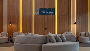 Un hall d’entrée moderne avec un grand canapé d’angle, des murs recouverts de panneaux en bois et une enseigne indiquant le restaurant « Rio in Samba ».
