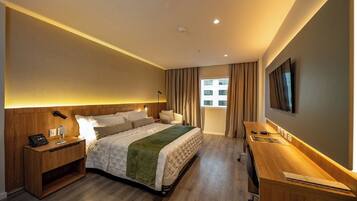 Une chambre d’hôtel équipée d’un lit, d’une table de chevet, d’un bureau, d’une chaise, d’une télévision et d’une fenêtre avec des rideaux.