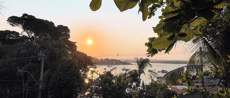 A sunset view from a balcony overlooking a body of water with boats, surrounded by dense foliage.