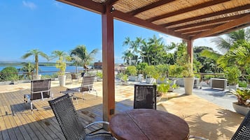 An outdoor patio with a thatched roof, wicker furniture, and a view of the sea.