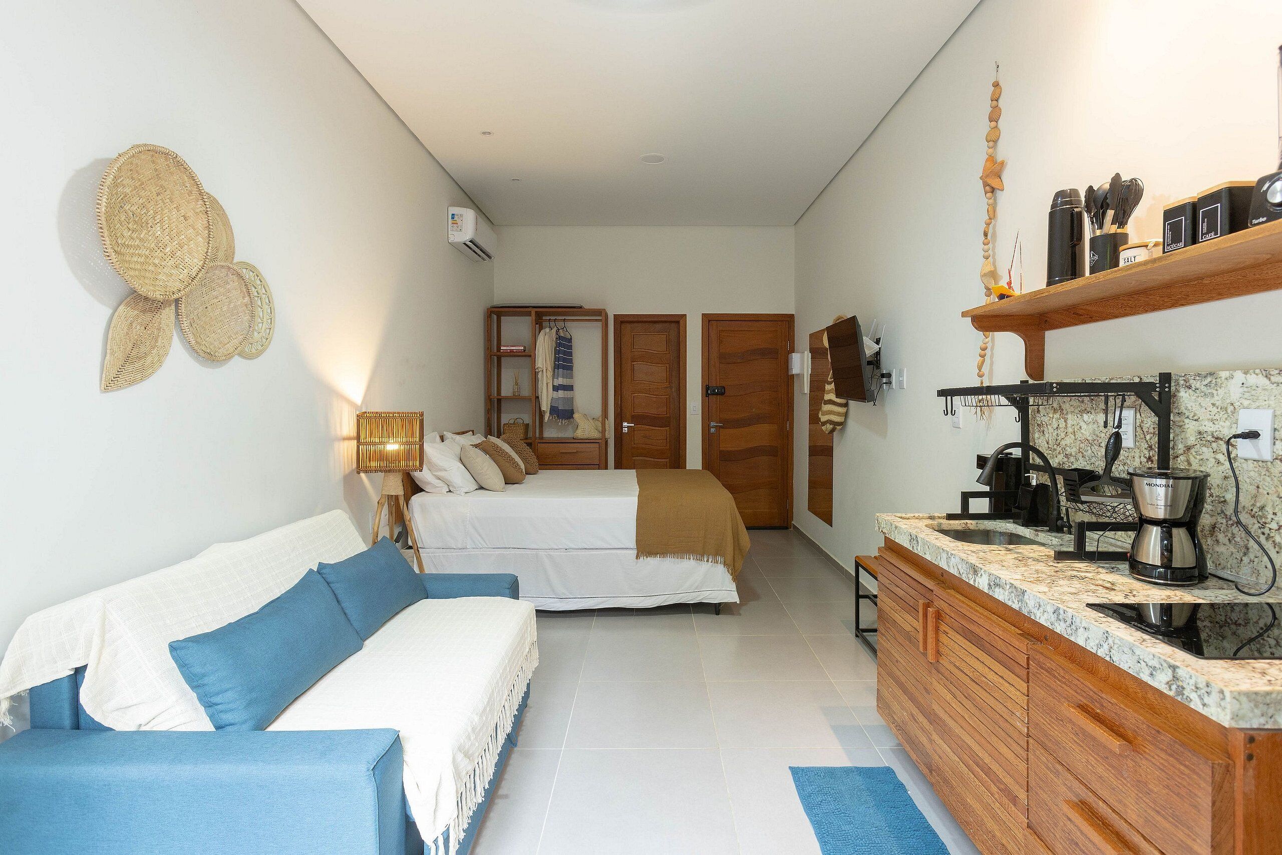 A bedroom with a bed, a sofa, a wooden cabinet, and a kitchen area with a coffee machine.