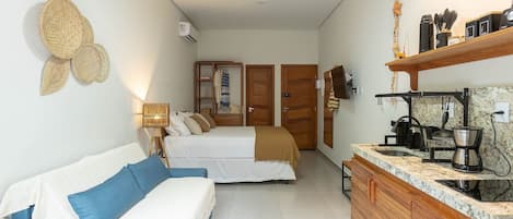 Quarto com cama, sofá, armário de madeira e espaço de cozinha com máquina de café.