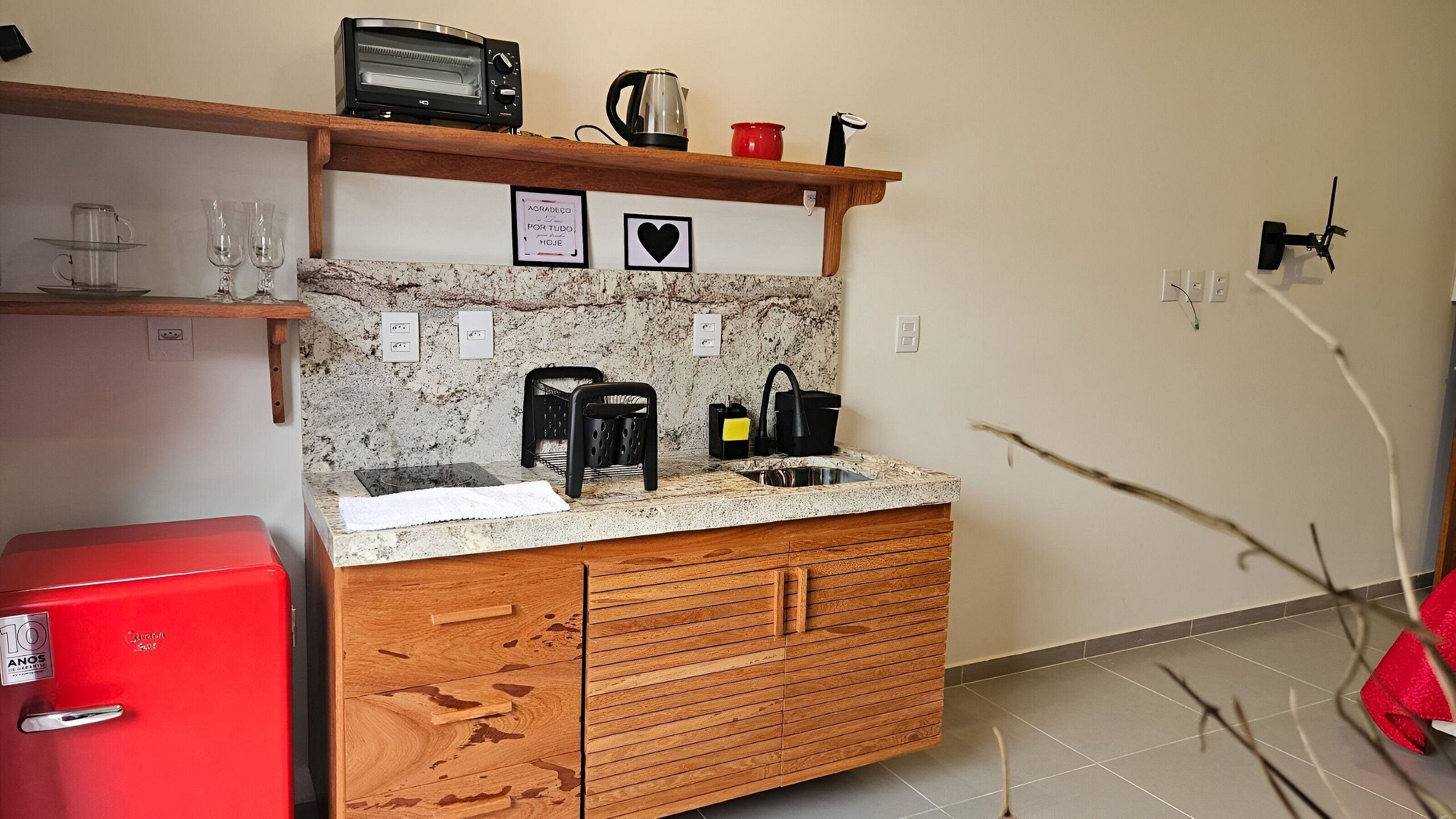 Cocina compacta con microondas, hervidor y cafetera sobre la encimera. Hay dos cuadros en la pared sobre el fregadero.