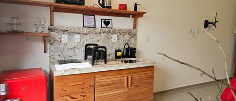 Cocina compacta con microondas, hervidor y cafetera sobre la encimera. Hay dos cuadros en la pared sobre el fregadero.