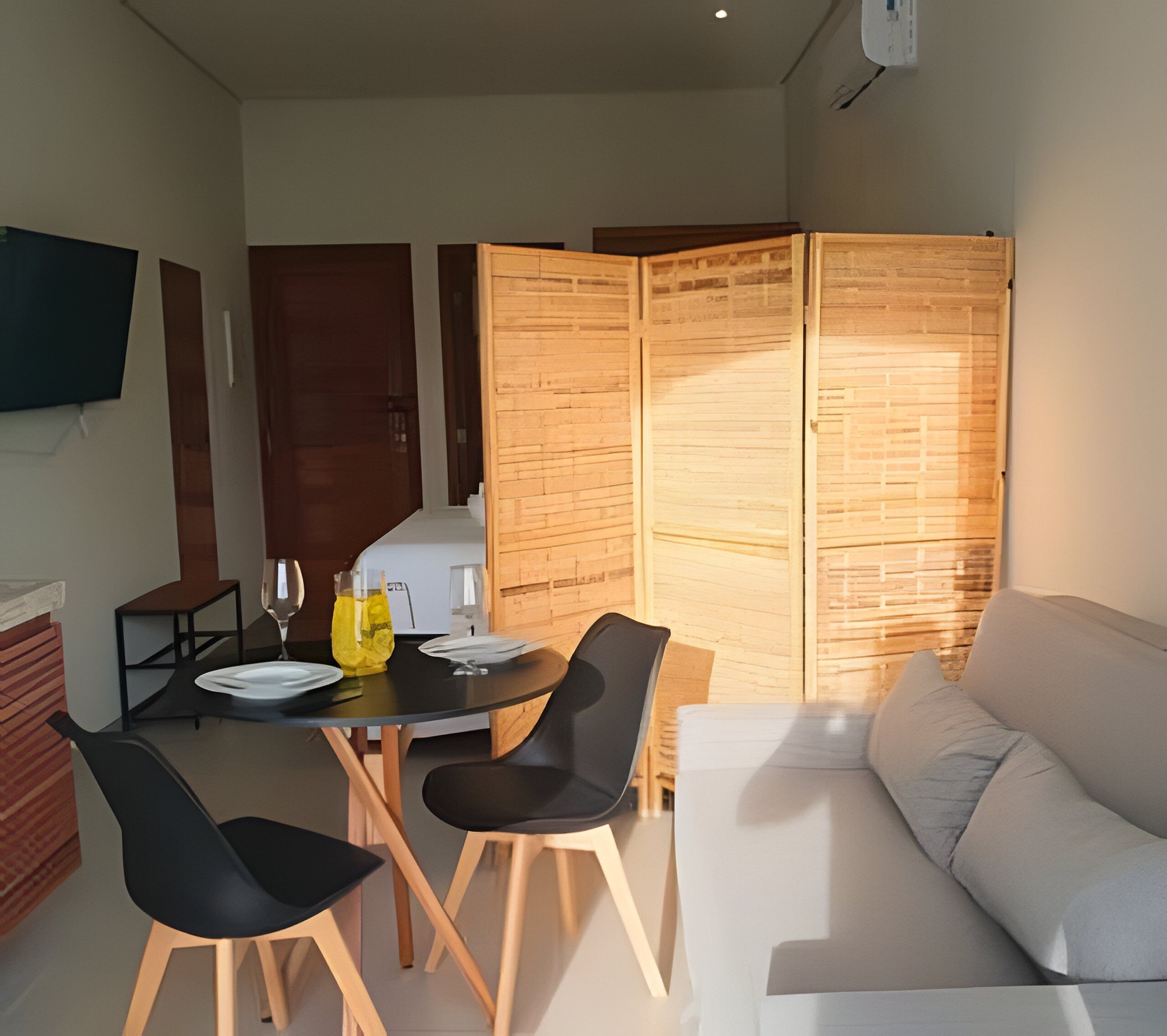 A modern living room with a dining area, a sofa, and a TV mounted on the wall.