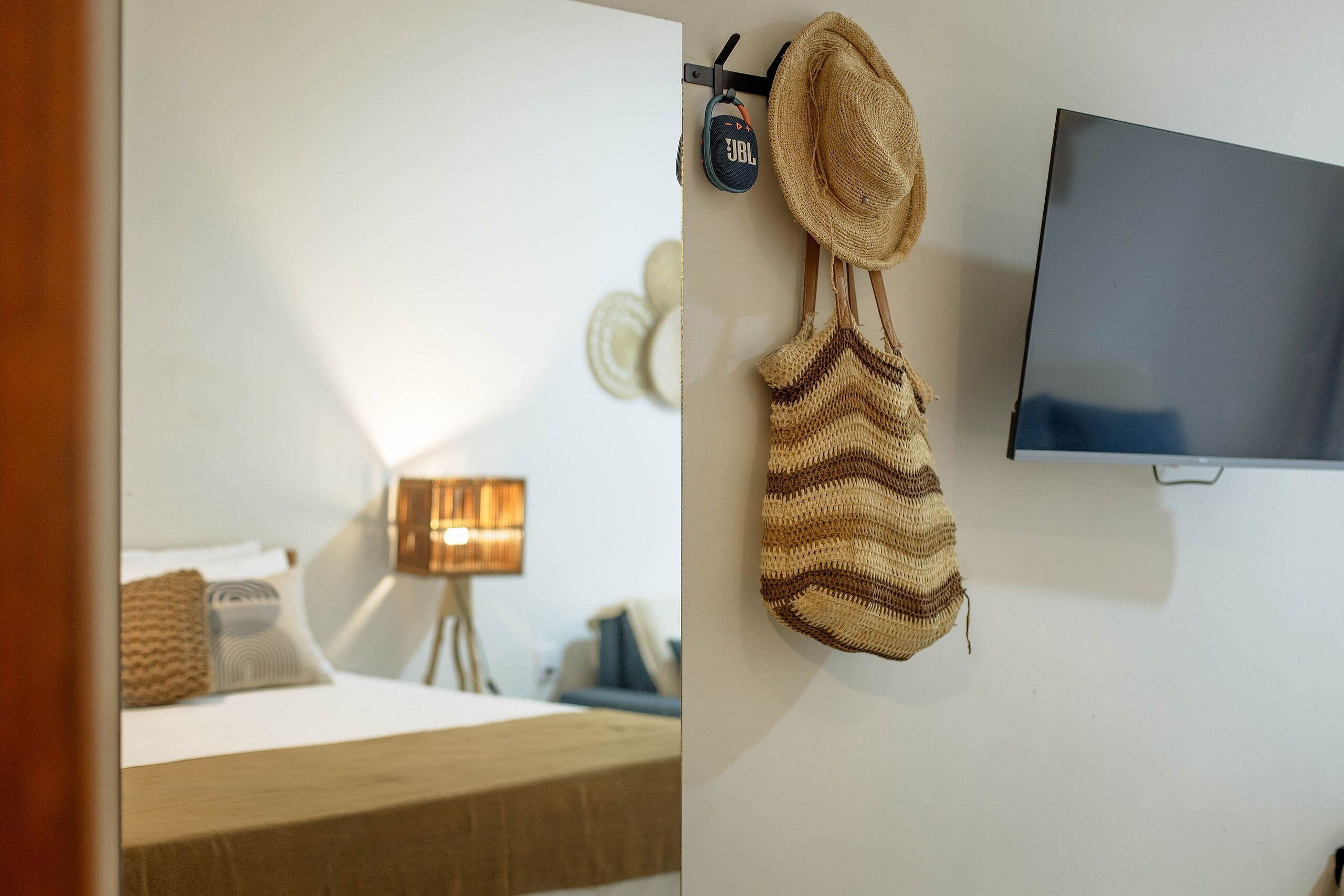 A hotel room with a bed, a TV mounted on the wall, and a woven bag hanging on the wall.