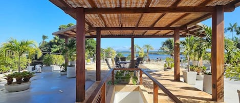 A covered outdoor area with a staircase leading to a higher level, surrounded by potted plants and a view of the sea.