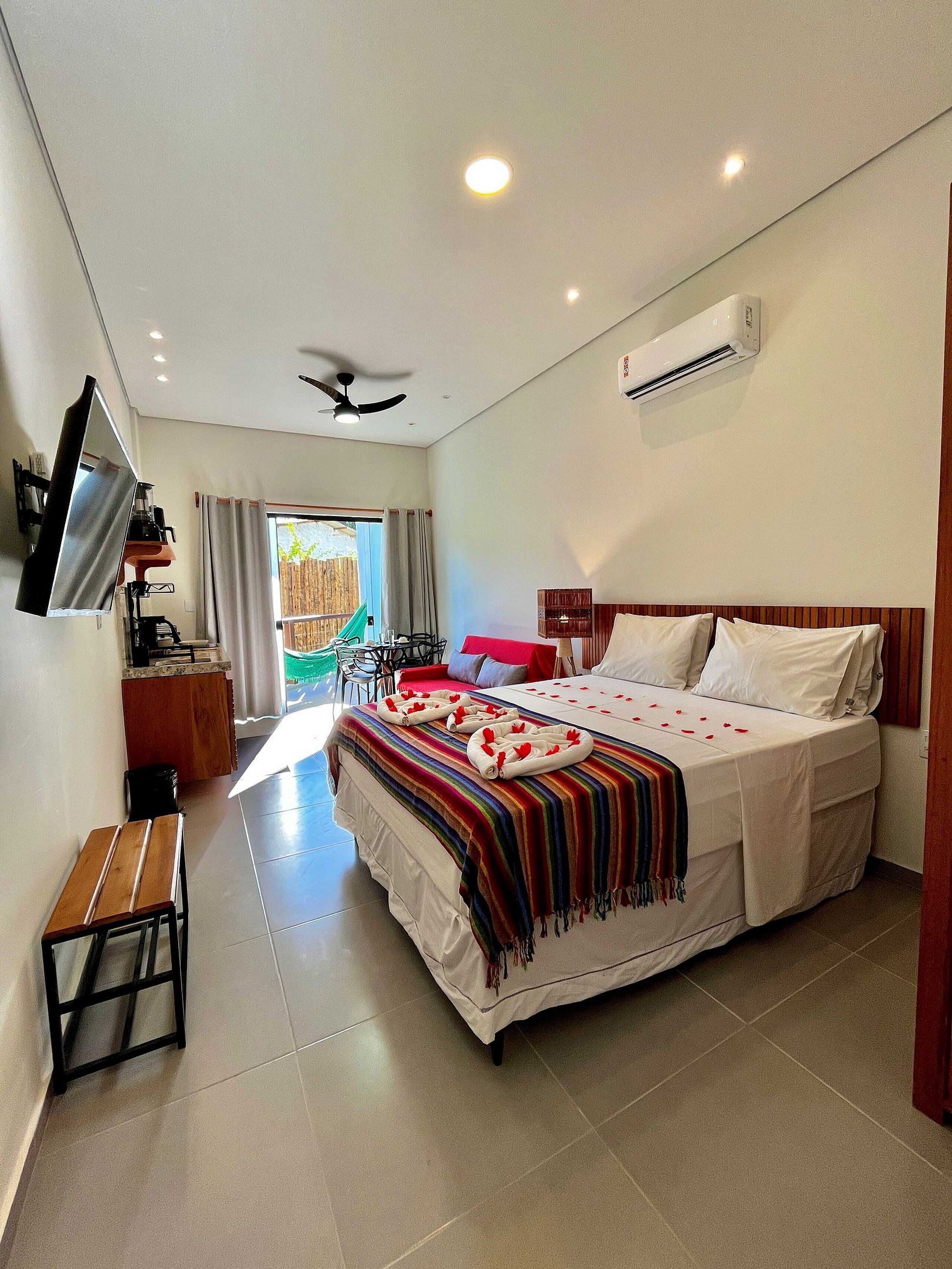 Une chambre d’hôtel équipée d’un lit, d’une télévision, d’un ventilateur de plafond, d’un climatiseur, d’une petite table et offrant une vue sur l’extérieur.