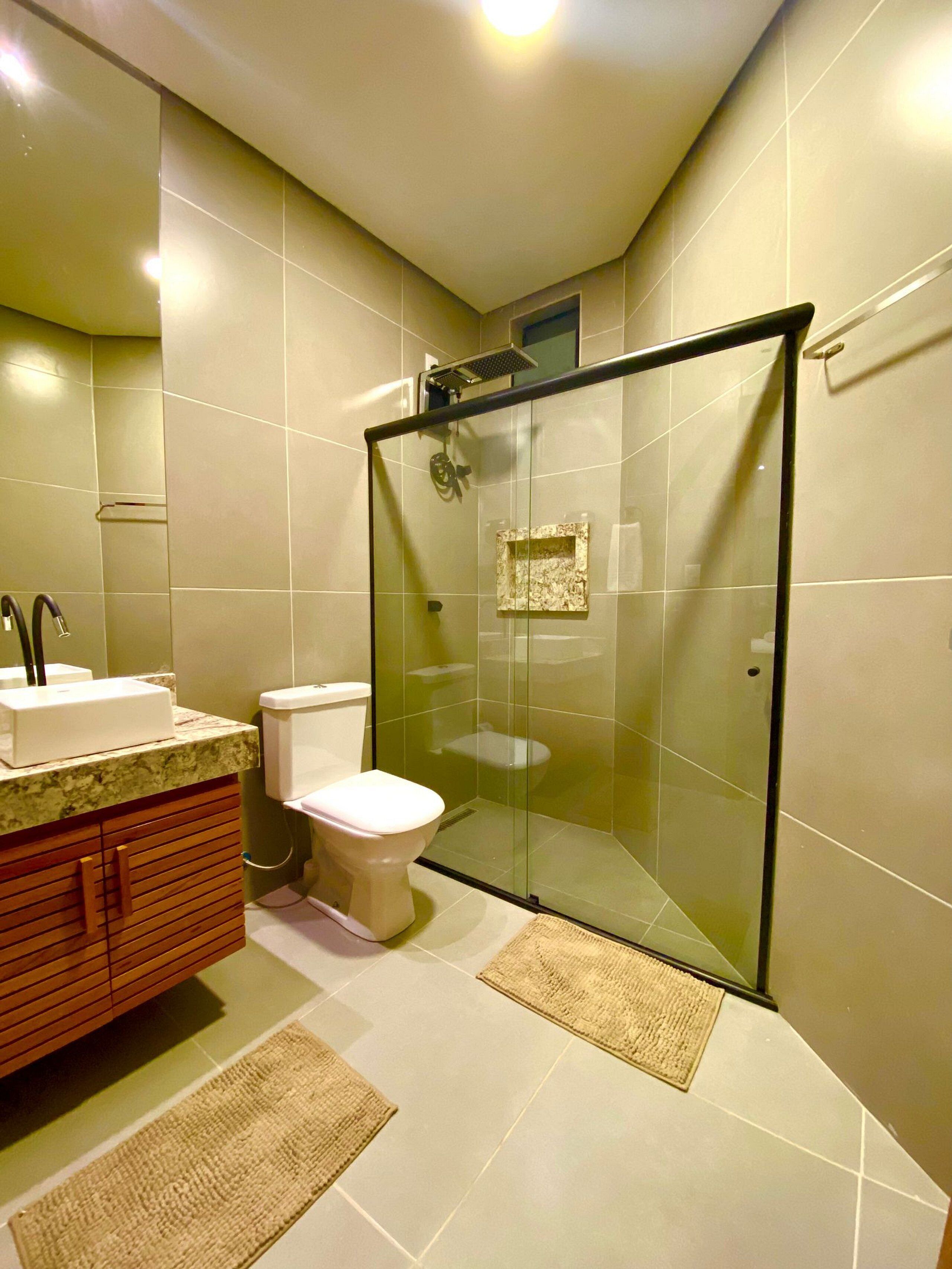 A modern bathroom with a glass-enclosed shower, a toilet, and a vanity with a sink and mirror.
