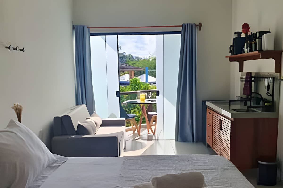 Quarto com cama, sofá, escrivaninha e vista para o exterior.
