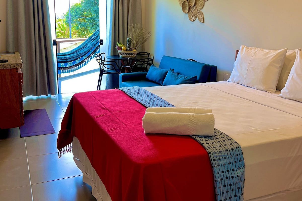 Quarto de hotel com uma cama, uma mesa de jantar com cadeiras, uma rede e vista para o verde lá fora.