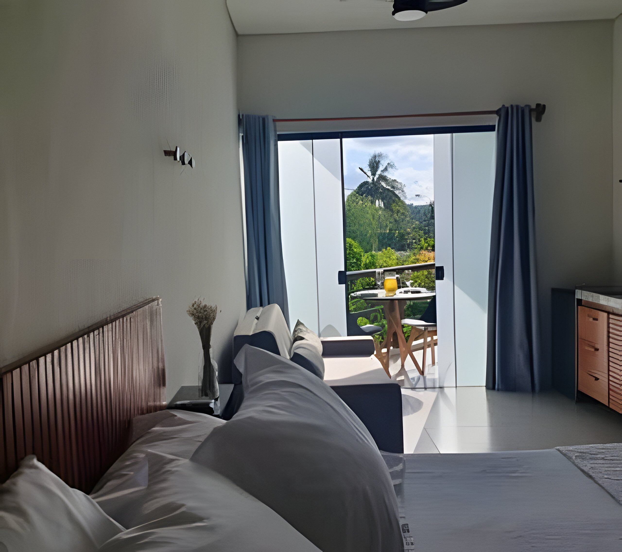 A bedroom with a bed, a nightstand, a vase with flowers, and a view of a balcony with a table and chairs.