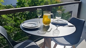 A balcony with a table set for two, featuring a pitcher of a yellow beverage, two wine glasses, and a water glass.