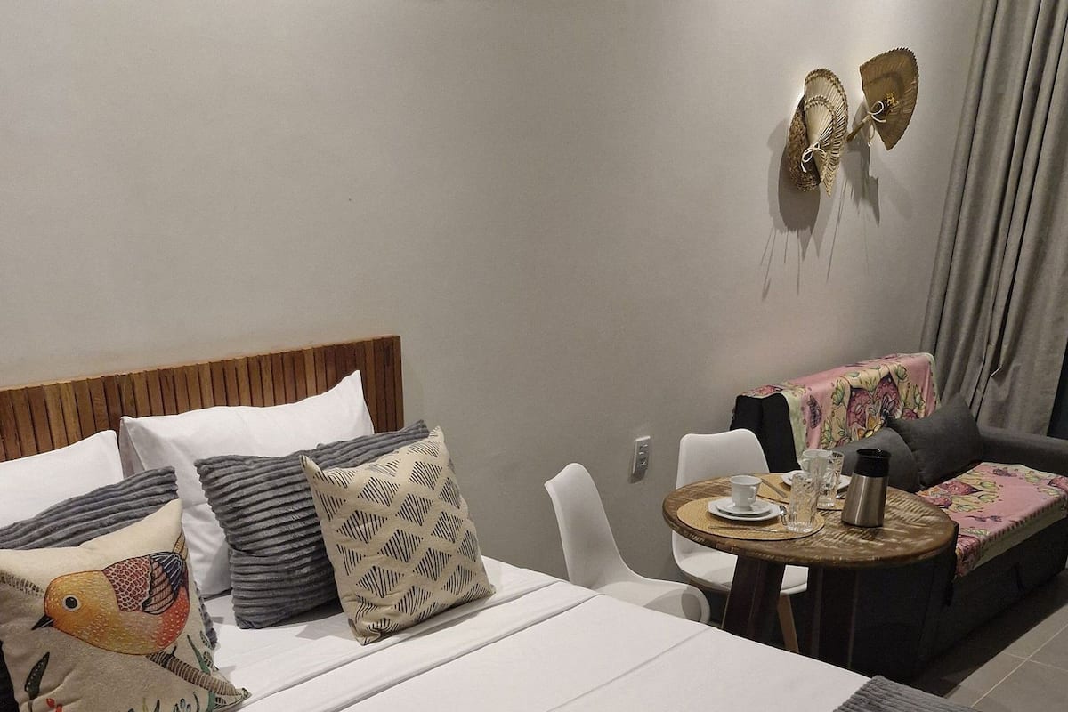 Quarto de hotel com uma cama, uma mesa redonda pequena com uma cafeteira e um sofá.