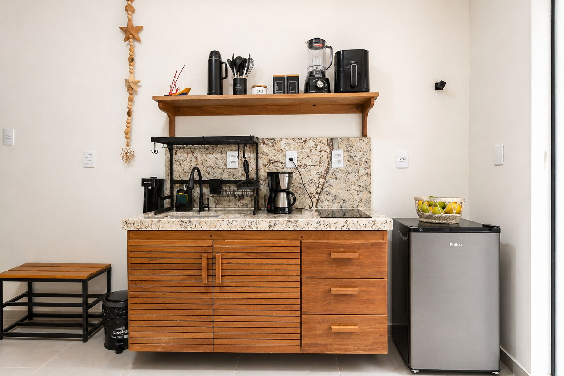 A compact kitchen with a marble countertop, wooden cabinets, a coffee maker, a blender, and a small refrigerator.