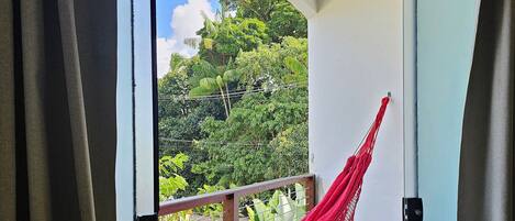 A room with a view of a lush green landscape, a red hammock, and a table with fruit.