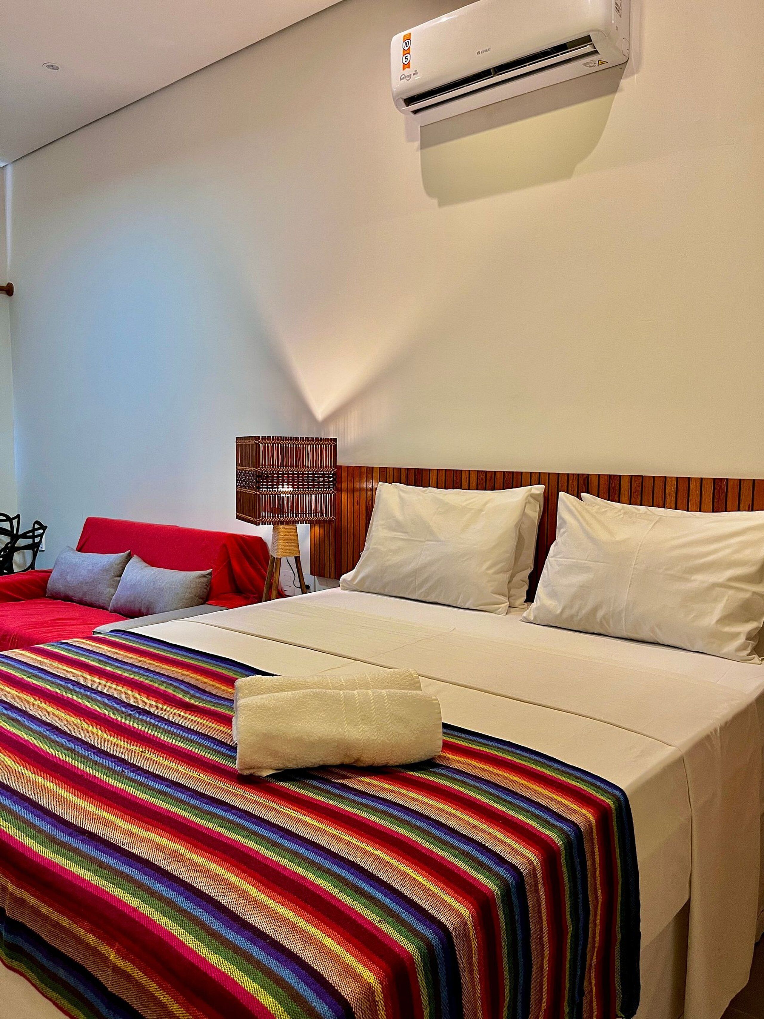 A hotel room with a bed, a red sofa, a lamp, and an air conditioning unit.