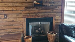 A wooden log fireplace with two baskets on either side, a small shelf above it, and a leather sofa to the right. - Charming 3-bedroom cottage in Oxford with WiFi and AC close to Wisconson Dells (Oxford)
