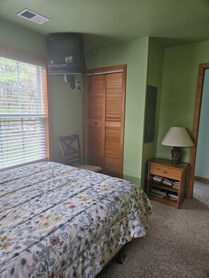 Un dormitorio con una cama, un armario de madera, un escritorio con una lámpara y una ventana con persianas.