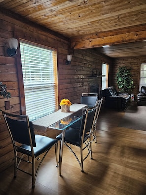 Interior de una cabaña de madera con una mesa de comedor, sillas y chimenea.