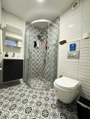 A bathroom with a shower enclosure, a toilet, a sink, and a mirror. - Ambers Alaçatı (Cesme)