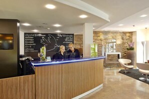 A reception area with a wooden reception desk, a stone wall, and a modern interior design. - Hotel Rutli (Zurich)