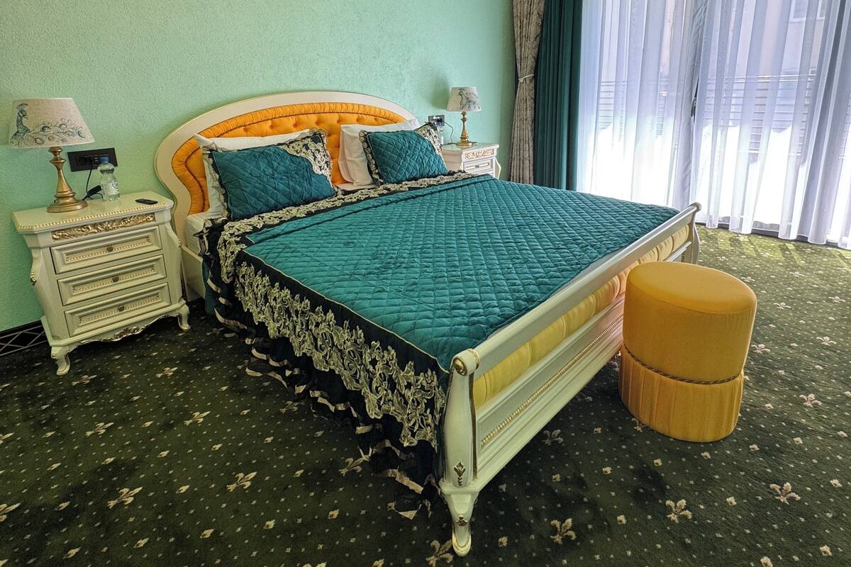 A bedroom with a bed, nightstands, a lamp, a window with curtains, and a patterned carpet.