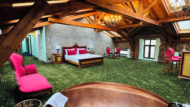 An attic bedroom with a large bathtub, a red chair, and a chandelier. - JMR Splendor-Private Sauna & Bathtub Sui (Constanta)