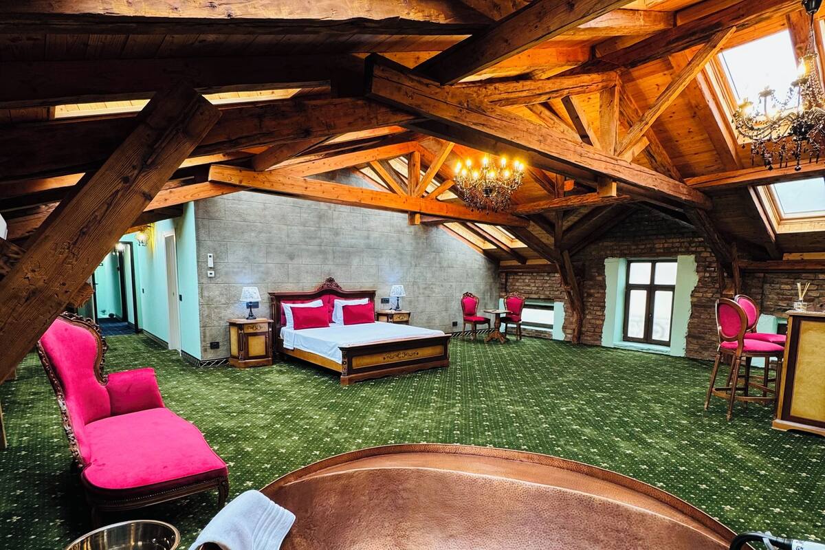 An attic bedroom with a large bathtub, a red chair, and a chandelier.