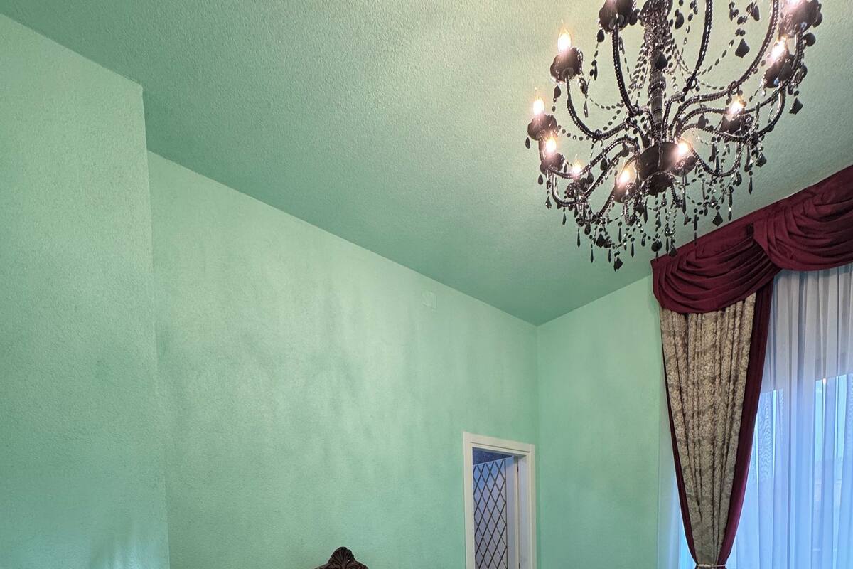 A bedroom with a bed, a nightstand, a chandelier, and a window with curtains.