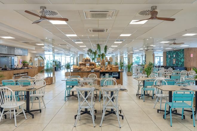Una amplia cafetería con numerosas mesas y sillas, ventiladores de techo y una zona de exhibición central.