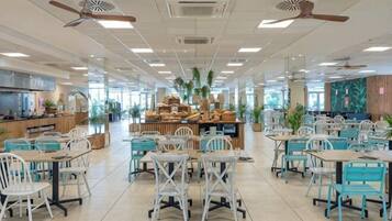 Una amplia cafetería con numerosas mesas y sillas, ventiladores de techo y una zona de exhibición central.