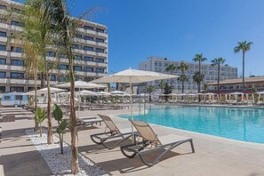 A pool area with lounge chairs and umbrellas, surrounded by palm trees and hotel buildings. - Innside Alcudia (Alcudia)