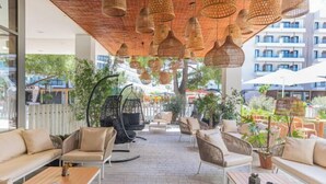 Un espace extérieur aménagé avec des meubles en osier, des lampes suspendues en osier et des plantes en pot.