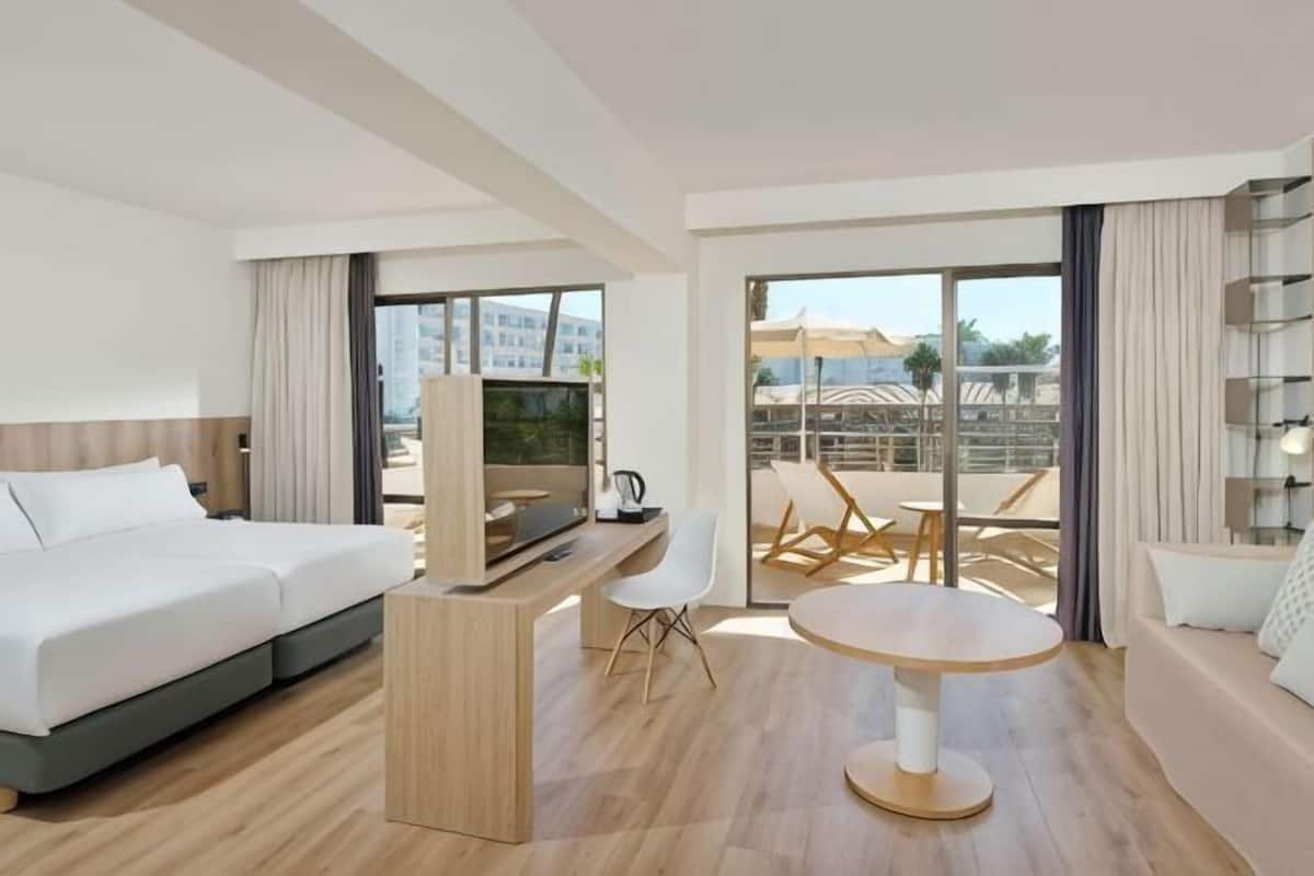 Quarto de hotel moderno com cama, televisão, escrivaninha e área de estar.