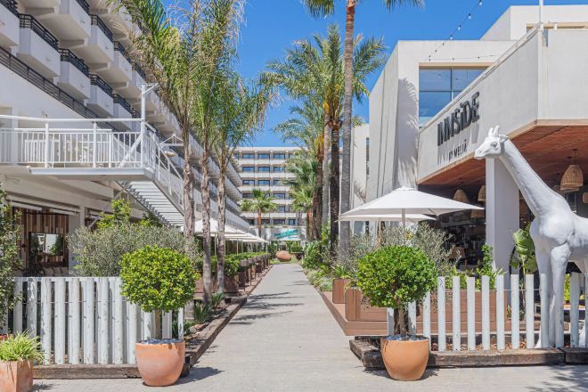 Un pasillo de hotel con una cerca blanca, plantas en macetas y una estatua de jirafa.