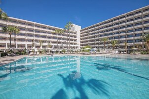 Un hotel con una piscina grande, varios pisos y palmeras.