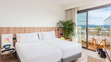 Habitación de hotel con dos camas, un escritorio, una silla, una planta y un balcón con vistas.