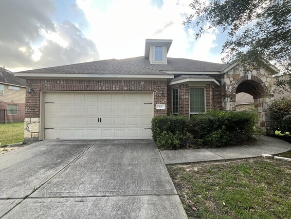 A two-story house with a garage, a stone archway, and a small porch. - Spacious 4 Bed/2 Bath Home in the Woodlands (Spring)