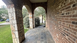 A covered walkway with stone columns and brick walls, leading to a grassy area. - Spacious 4 Bed/2 Bath Home in the Woodlands (Spring)