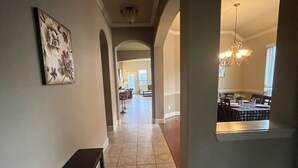 A hallway with a bench, a dining area with a chandelier, and a kitchen visible through an archway. - Spacious 4 Bed/2 Bath Home in the Woodlands (Spring)