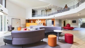Un hall d’entrée spacieux, doté de sièges modernes, d’un mur d’accent orange qui attire l’attention et d’une mezzanine avec une rambarde.