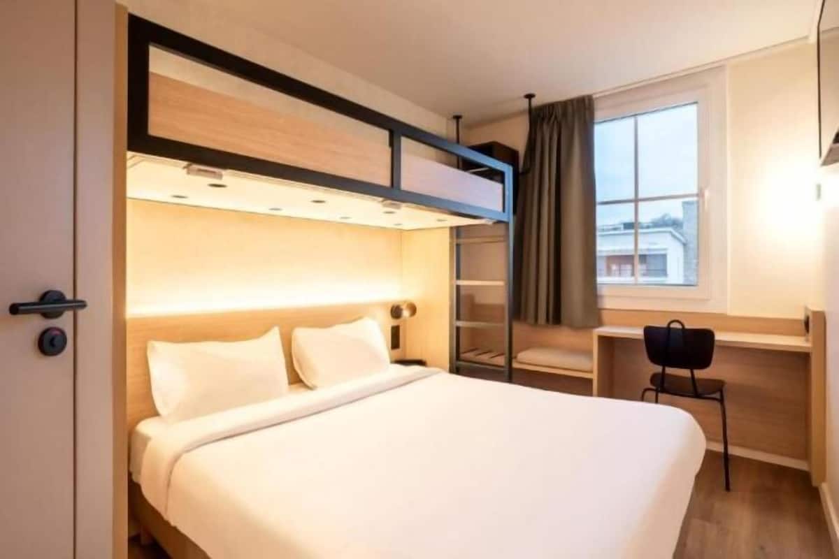 Ein Hotelzimmer mit einem Etagenbett, einem Schreibtisch, einem Stuhl und einem Vorhangfenster.