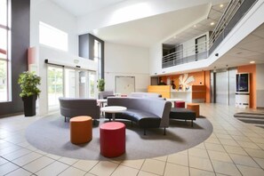 Eine großzügige Lobby mit einer gebogenen Sitzecke, einem Empfangsbereich und einer Treppe, die in eine obere Etage führt.